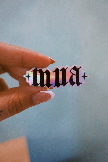 Hand holding a colorful 'mua' sticker against a light blue background