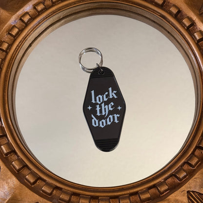 Black keychain with 'lock the door' text on a reflective surface with a decorative frame.