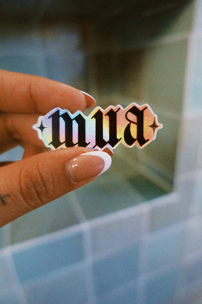 Hand holding a holographic 'mua' sticker against a blurred background