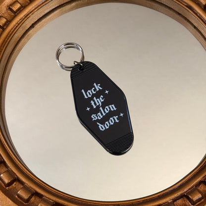 Black keychain with 'lock the salon door' text on a mirror surface