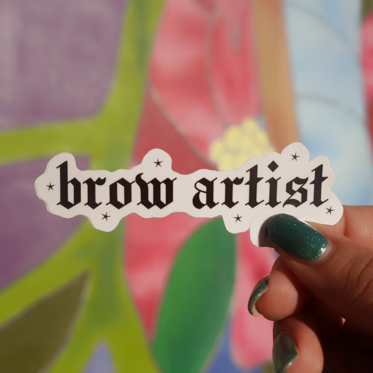 Hand holding a 'brow artist' sticker with colorful background