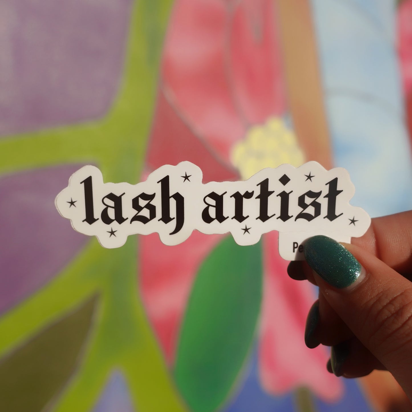 Sticker with 'lash artist' text held by a hand against a colorful background