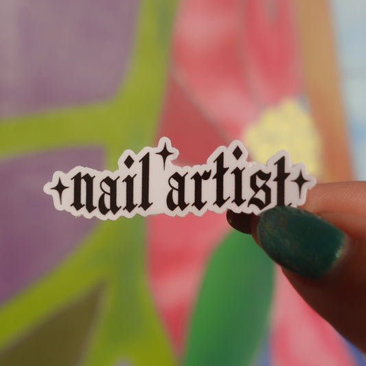Sticker with 'nail artist' text held by a hand with green nail polish against a colorful abstract background.