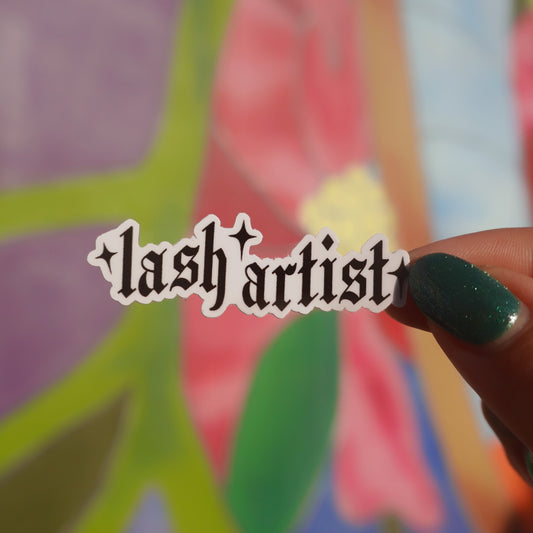 Hand holding a 'lash artist' sticker in front of colorful abstract art