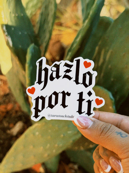 Hand holding a sticker with 'hazlo por ti' text in front of a cactus plant